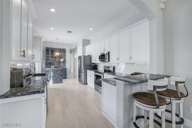 kitchen with tasteful backsplash, white cabinets, appliances with stainless steel finishes, dark stone countertops, and a sink