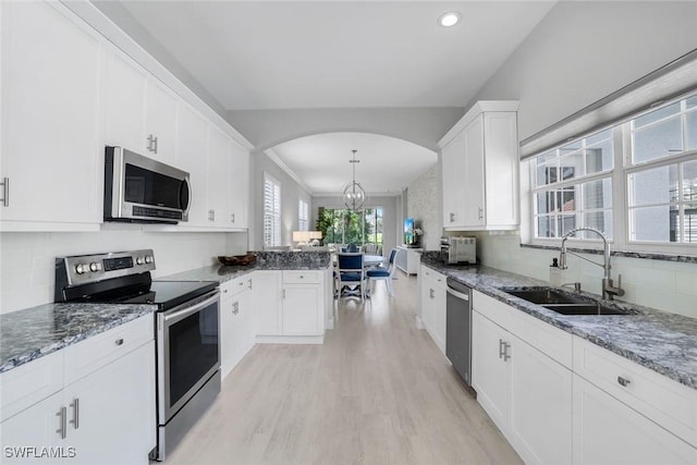 kitchen featuring white cabinets, light wood-style flooring, a sink, stainless steel appliances, and backsplash