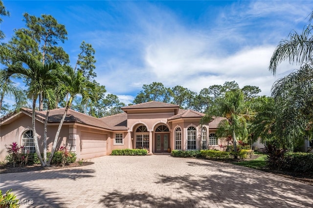 mediterranean / spanish home featuring a garage, french doors, decorative driveway, and stucco siding