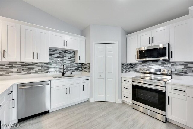 kitchen featuring stainless steel appliances, light countertops, white cabinets, vaulted ceiling, and a sink