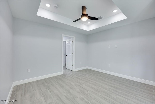 unfurnished room featuring a raised ceiling, visible vents, light wood-style flooring, and baseboards