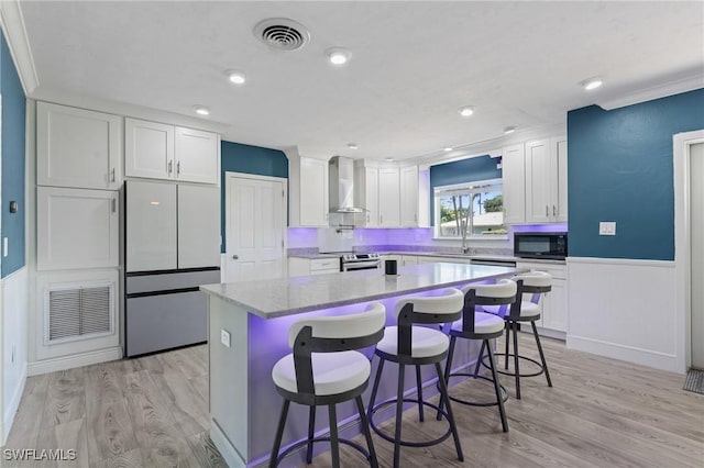 kitchen with wall chimney exhaust hood, white cabinetry, visible vents, and refrigerator