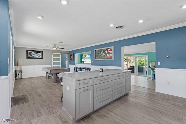 kitchen featuring visible vents, a wainscoted wall, a kitchen island, crown molding, and light wood-style floors