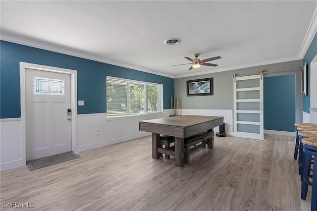 dining area with light wood finished floors, visible vents, a barn door, wainscoting, and ceiling fan