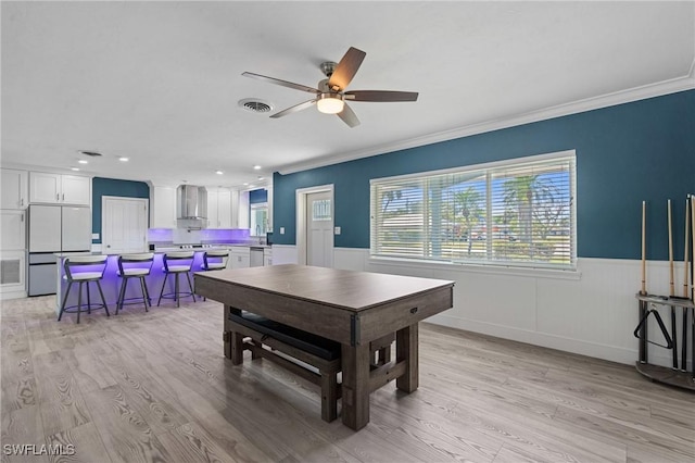 dining area with light wood-style flooring, visible vents, a ceiling fan, wainscoting, and crown molding