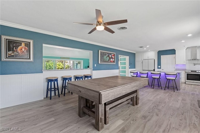 game room featuring a wainscoted wall, crown molding, visible vents, light wood-style flooring, and a ceiling fan