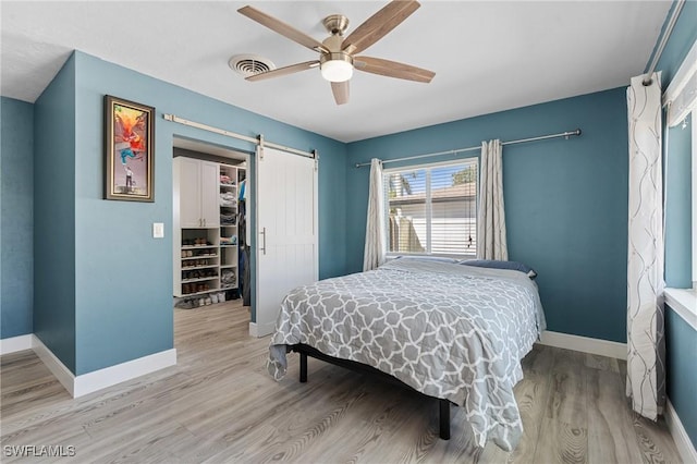 bedroom featuring a barn door, light wood-type flooring, visible vents, and baseboards