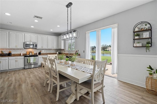 dining space featuring light wood-type flooring, a water view, visible vents, and recessed lighting