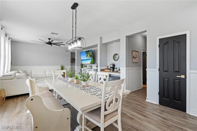 dining room featuring ceiling fan, visible vents, wood finished floors, and wainscoting