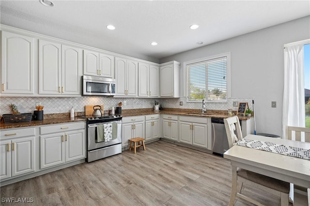 kitchen featuring stainless steel appliances, light wood-style flooring, white cabinets, a sink, and dark stone countertops