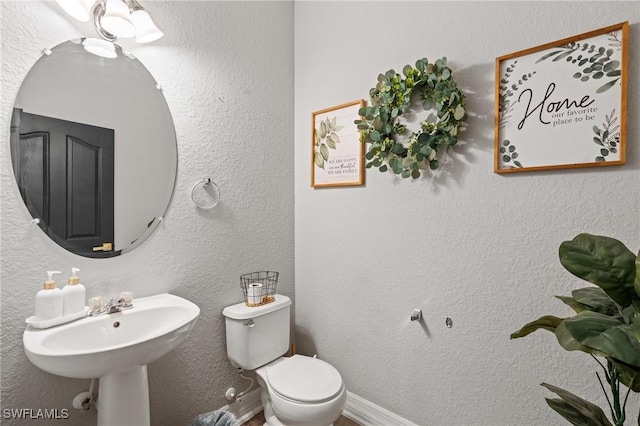 half bath featuring toilet, baseboards, a sink, and a textured wall