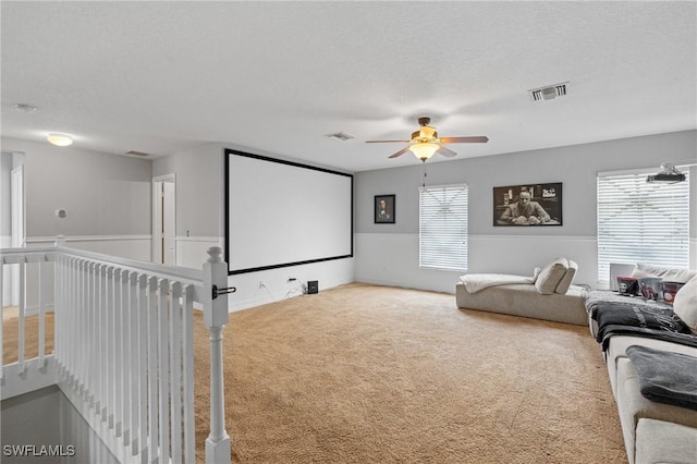 carpeted home theater room featuring a textured ceiling, ceiling fan, and visible vents