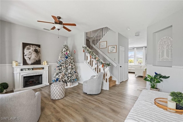 living room featuring visible vents, stairway, a premium fireplace, ceiling fan, and wood finished floors