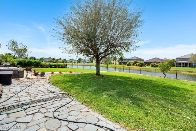 view of community with a water view, fence, a lawn, and a patio