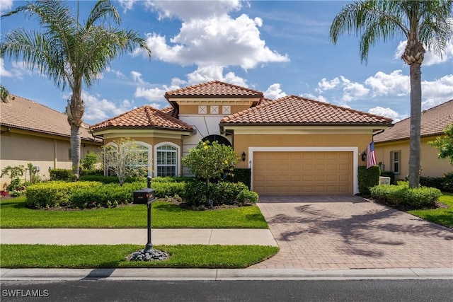 mediterranean / spanish house featuring a garage, decorative driveway, a tiled roof, and stucco siding