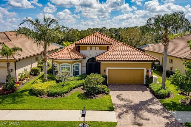 mediterranean / spanish home with a garage, stucco siding, a tile roof, decorative driveway, and a front yard