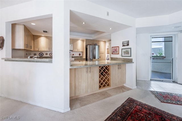 kitchen featuring visible vents, white microwave, light brown cabinets, and freestanding refrigerator