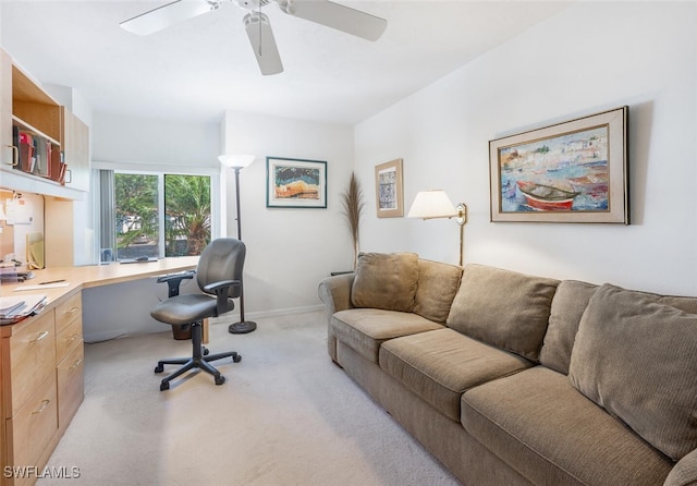 office area featuring light carpet, baseboards, a ceiling fan, and built in desk