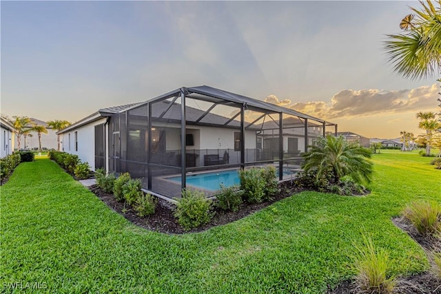 pool at dusk with glass enclosure, an outdoor pool, and a lawn