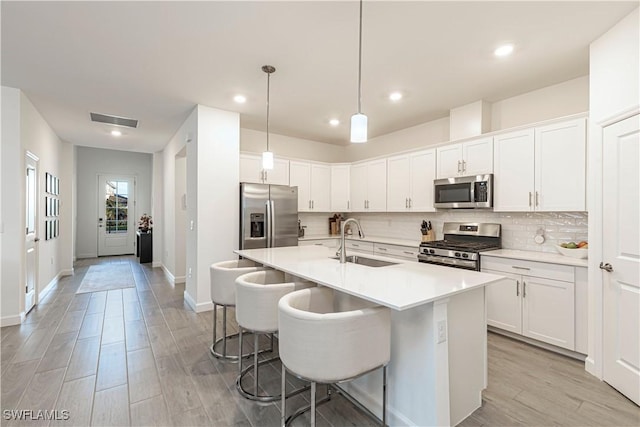 kitchen featuring visible vents, decorative backsplash, appliances with stainless steel finishes, a kitchen breakfast bar, and a sink