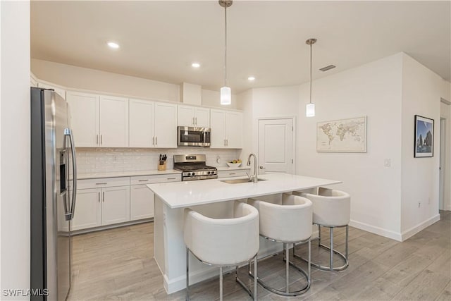 kitchen featuring light wood finished floors, tasteful backsplash, visible vents, appliances with stainless steel finishes, and a sink