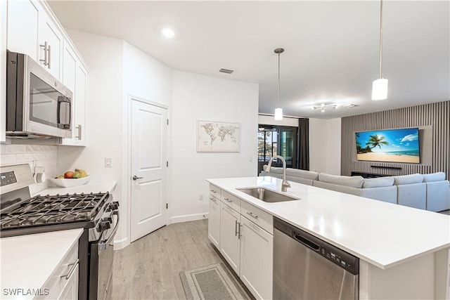 kitchen with appliances with stainless steel finishes, white cabinets, a sink, and light wood finished floors