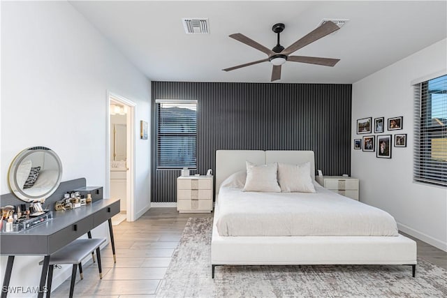 bedroom with visible vents, an accent wall, connected bathroom, wood finished floors, and baseboards