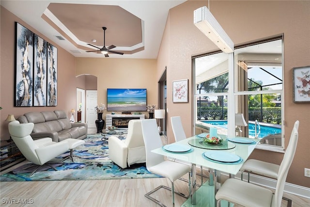 living room featuring ceiling fan, a fireplace, wood finished floors, visible vents, and a raised ceiling