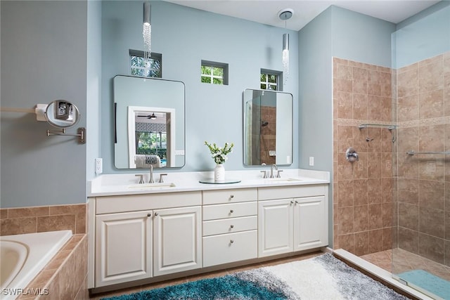 bathroom with double vanity, a relaxing tiled tub, a tile shower, and a sink