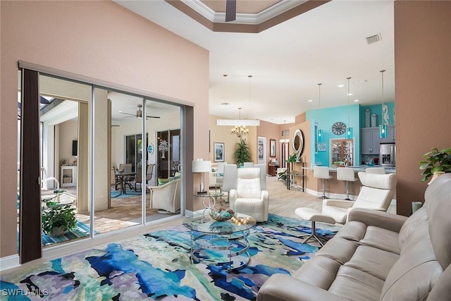 living room featuring ceiling fan with notable chandelier, visible vents, baseboards, light wood-type flooring, and crown molding