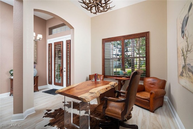 dining room with arched walkways, light wood-style flooring, baseboards, and an inviting chandelier