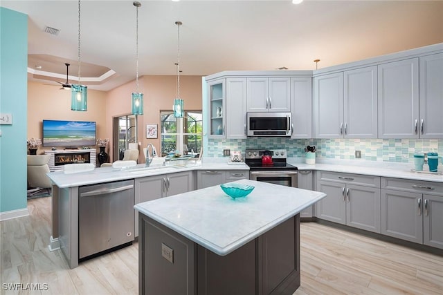 kitchen with a raised ceiling, appliances with stainless steel finishes, a peninsula, gray cabinets, and a sink