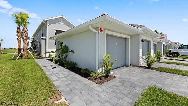 view of property exterior featuring an attached garage, a yard, decorative driveway, and stucco siding