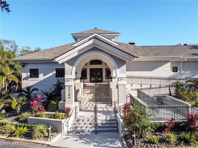 view of front facade with stucco siding, fence, stairway, and french doors