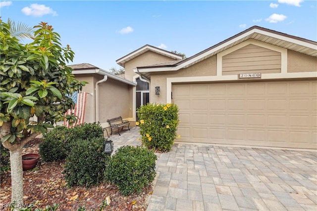 view of front of house featuring decorative driveway, an attached garage, and stucco siding