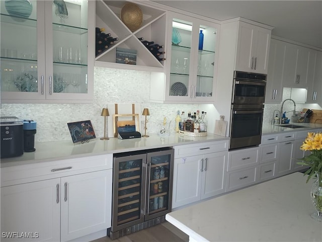 bar featuring wine cooler, decorative backsplash, double oven, a sink, and a bar