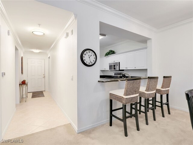 kitchen featuring a breakfast bar area, light colored carpet, ornamental molding, appliances with stainless steel finishes, and dark countertops