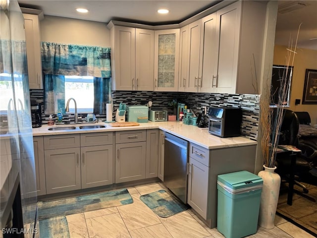 kitchen featuring stainless steel dishwasher, tasteful backsplash, gray cabinets, and a sink