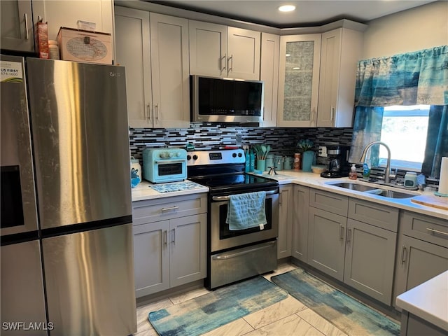 kitchen with a sink, light countertops, stainless steel appliances, gray cabinetry, and backsplash