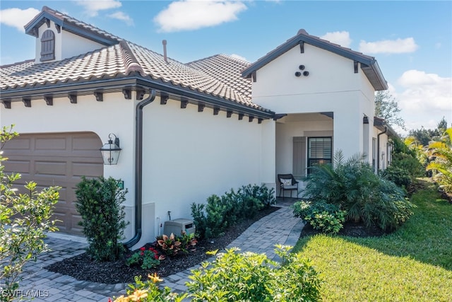 mediterranean / spanish-style house featuring a tiled roof, a front yard, an attached garage, and stucco siding