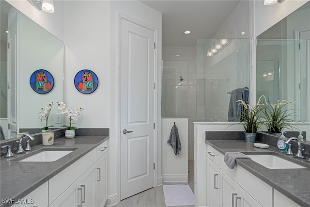 bathroom with a tile shower, two vanities, and a sink