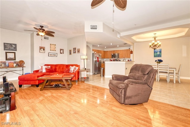 living room featuring light wood-type flooring, a raised ceiling, visible vents, and ceiling fan with notable chandelier