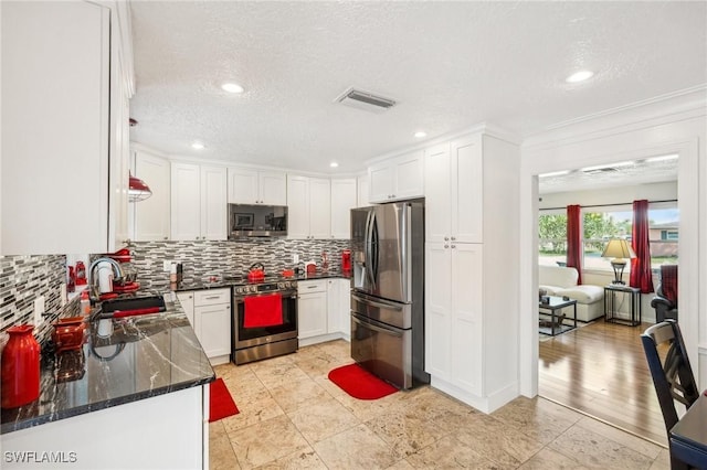 kitchen with a sink, visible vents, white cabinets, appliances with stainless steel finishes, and backsplash