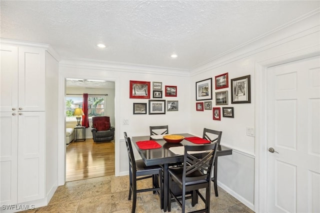 dining room featuring a textured ceiling, baseboards, stone tile flooring, and crown molding