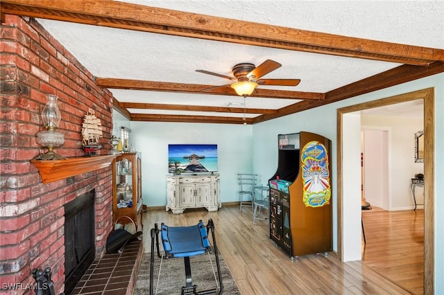 living room featuring beam ceiling, a brick fireplace, ceiling fan, a textured ceiling, and wood finished floors