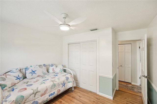 bedroom with a closet, visible vents, light wood-style floors, ceiling fan, and a textured ceiling