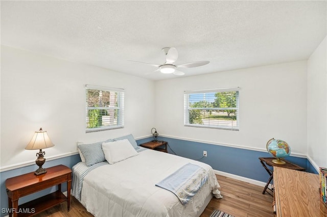 bedroom featuring multiple windows, a textured ceiling, baseboards, and wood finished floors