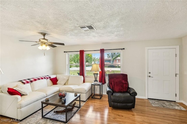 living area featuring visible vents, a ceiling fan, a textured ceiling, baseboards, and hardwood / wood-style flooring