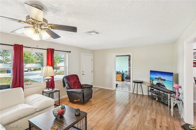 living room with baseboards, visible vents, ceiling fan, a textured ceiling, and light wood-style floors