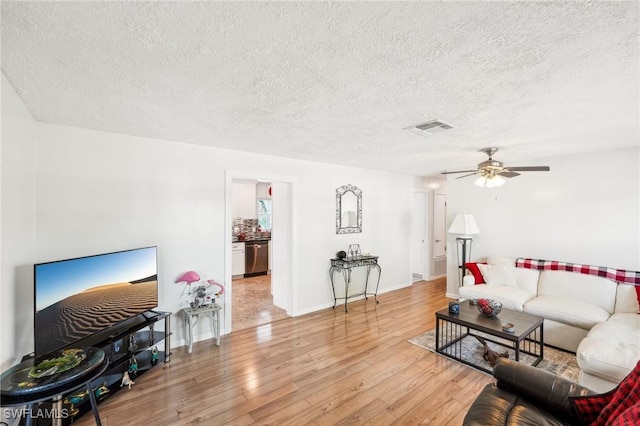 living area with visible vents, light wood-style floors, ceiling fan, a textured ceiling, and baseboards